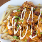 BBQ chicken fries with melted cheese, bacon, and scallions on a white plate