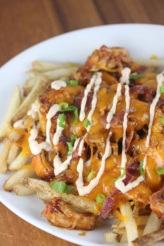 BBQ chicken fries with melted cheese, bacon, and scallions on a white plate