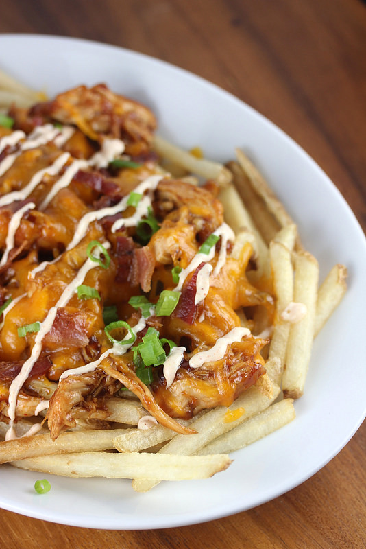 BBQ chicken fries with melted cheese, bacon, and scallions on a white plate