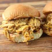 Pulled pork sandwich with mustard barbecue sauce spilling out of a bun on a wooden board