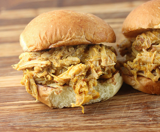 Pulled pork sandwich with mustard barbecue sauce spilling out of a bun on a wooden board