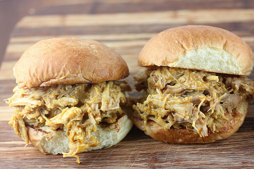 Pulled pork sandwich with mustard barbecue sauce spilling out of a bun on a wooden board