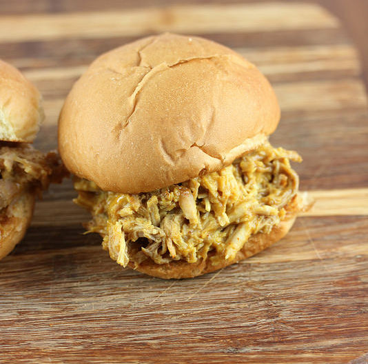 Pulled pork sandwich with mustard barbecue sauce spilling out of a bun on a wooden board