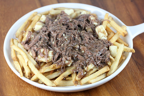 Plate of French fries topped with shredded short ribs and melted cheese curds