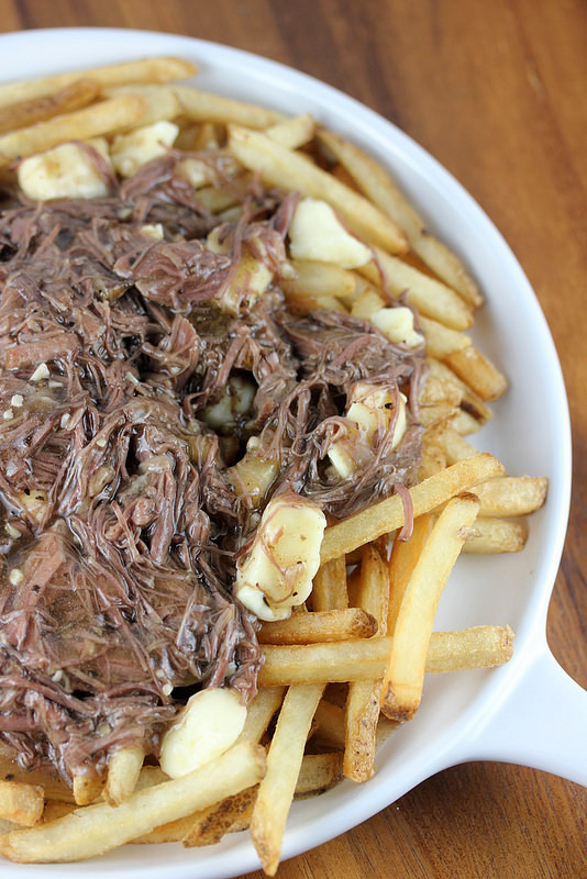 Plate of French fries topped with shredded short ribs and melted cheese curds