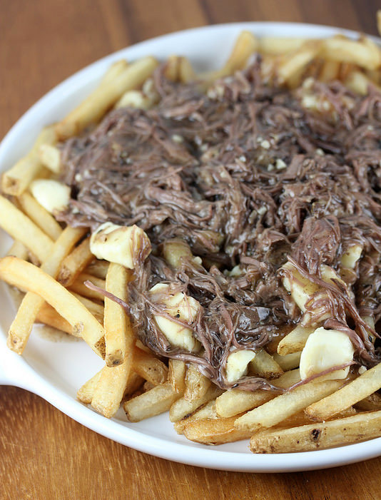 Plate of French fries topped with shredded short ribs and melted cheese curds