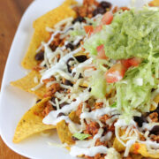 Plate of nachos topped with seasoned chicken, lettuce, tomato, cheese, and guacamole