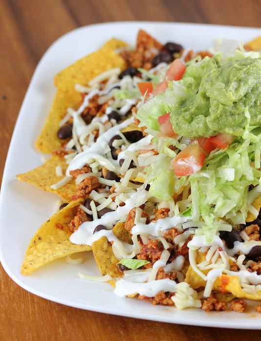 Plate of nachos topped with seasoned chicken, lettuce, tomato, cheese, and guacamole
