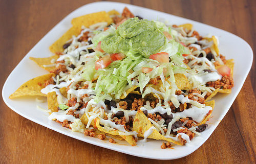 Plate of nachos topped with seasoned chicken, lettuce, tomato, cheese, and guacamole