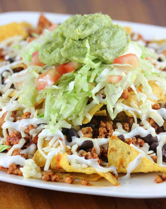 Plate of nachos topped with seasoned chicken, lettuce, tomato, cheese, and guacamole