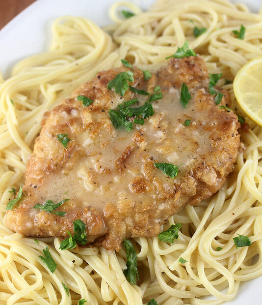 French chicken with lemon butter sauce served over pasta and garnished with parsley