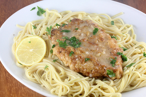 French chicken with lemon butter sauce served over pasta and garnished with parsley