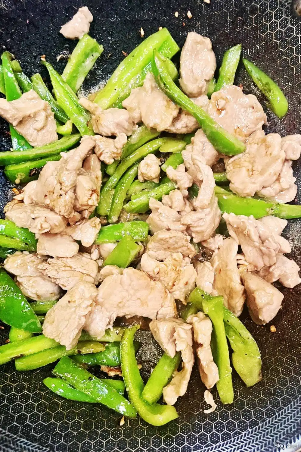 Pork and bell peppers cooking in a wok.