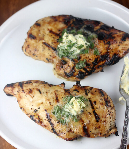 Grilled chicken breast topped with herb butter on a white plate