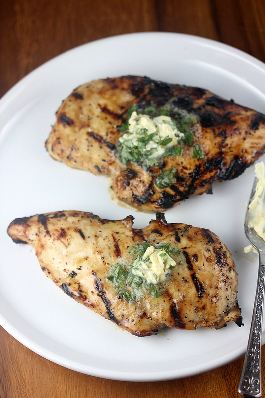 Grilled chicken breast topped with herb butter on a white plate
