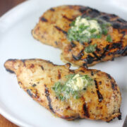 Grilled chicken breast topped with herb butter on a white plate