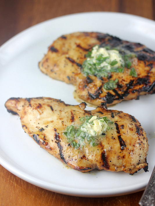 Grilled chicken breast topped with herb butter on a white plate