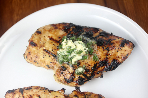 Grilled chicken breast topped with herb butter on a white plate