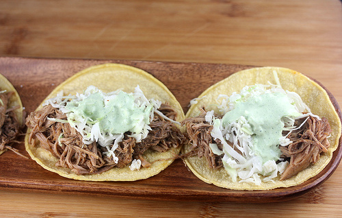 Corn tortilla topped with shredded pork, shredded cabbage, and creamy green sauce