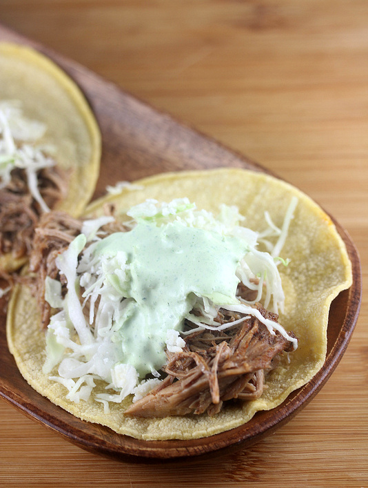 Corn tortilla topped with shredded pork, shredded cabbage, and creamy green sauce