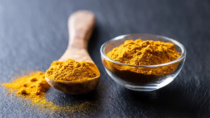 Indian turmeric powder in a bowl and wooden spoon.
