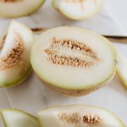 Sliced limelon halves and wedges on a white cutting board with visible seeds in the center
