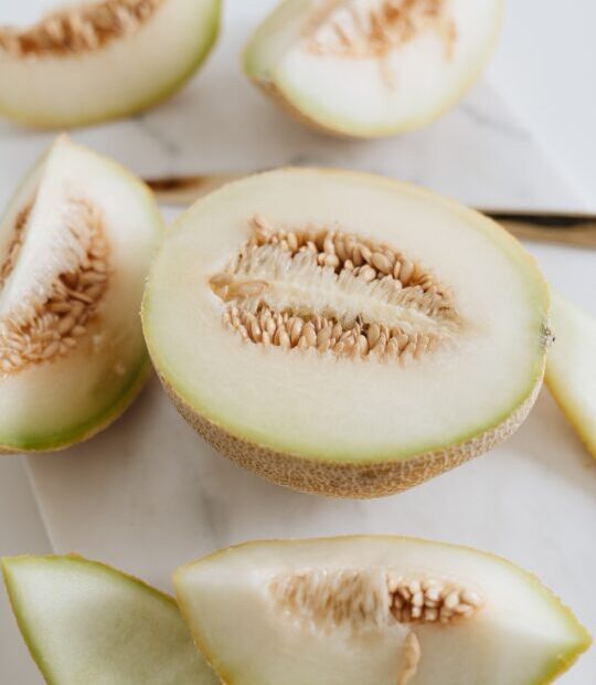 Sliced limelon halves and wedges on a white cutting board with visible seeds in the center