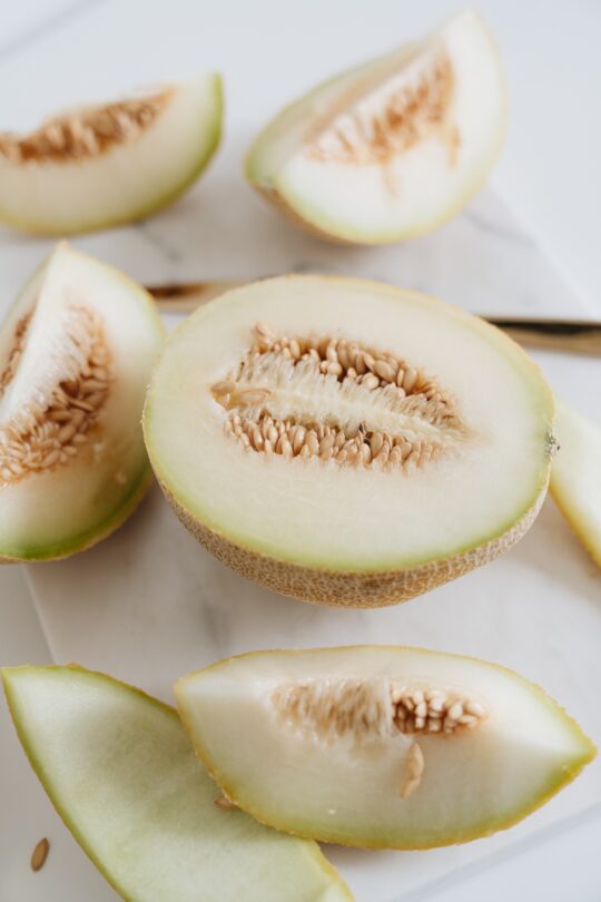 Sliced limelon halves and wedges on a white cutting board with visible seeds in the center