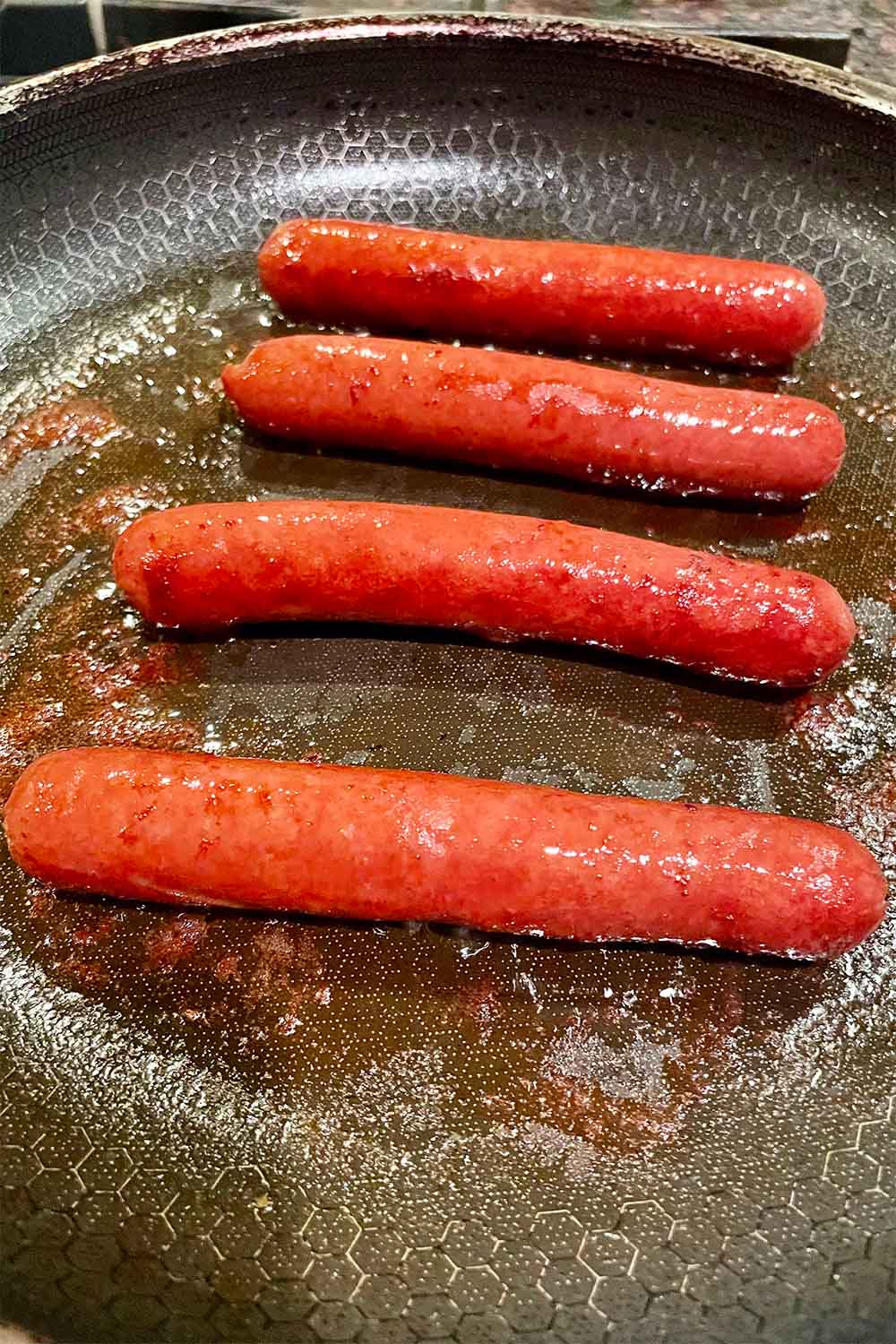 Hot dogs cooking in a pan on the stove.