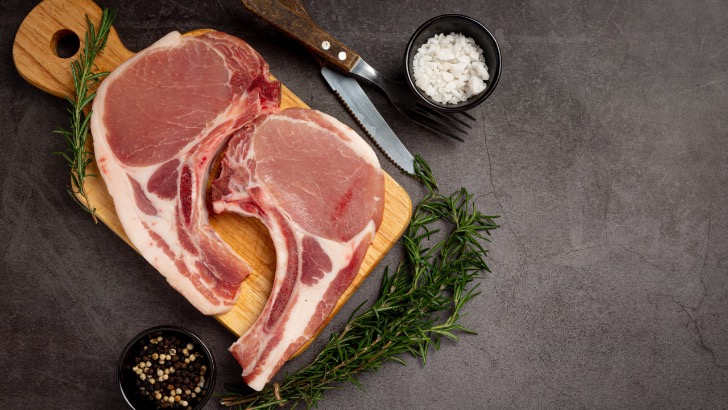 Top view of raw, bone-in pork chops on cutting board.