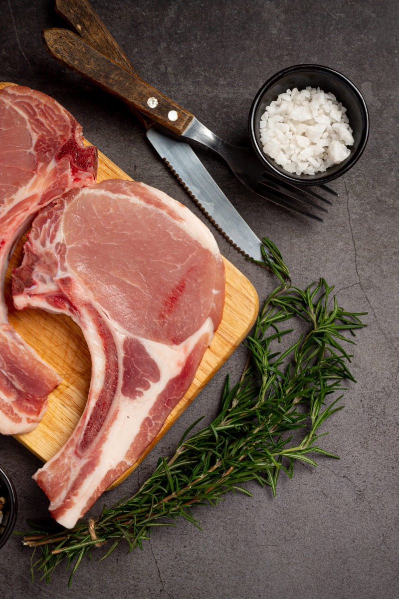 Top view of raw, bone-in pork chops on cutting board.