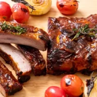 Prepared, oven-baked ribs with tomatoes on serving board.