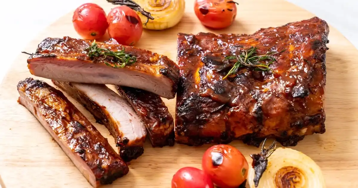 Prepared, oven-baked ribs with tomatoes on serving board.