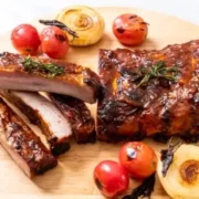 Prepared, oven-baked ribs with tomatoes on serving board.