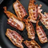 Overhead view of cooked bacon strips in skillet.