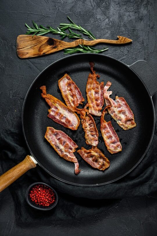 Overhead view of cooked bacon strips in skillet.