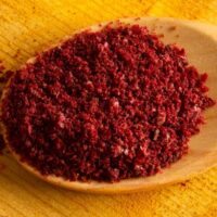 Ground sumac in a spoon on wooden table.