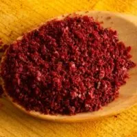 Ground sumac in a spoon on wooden table.