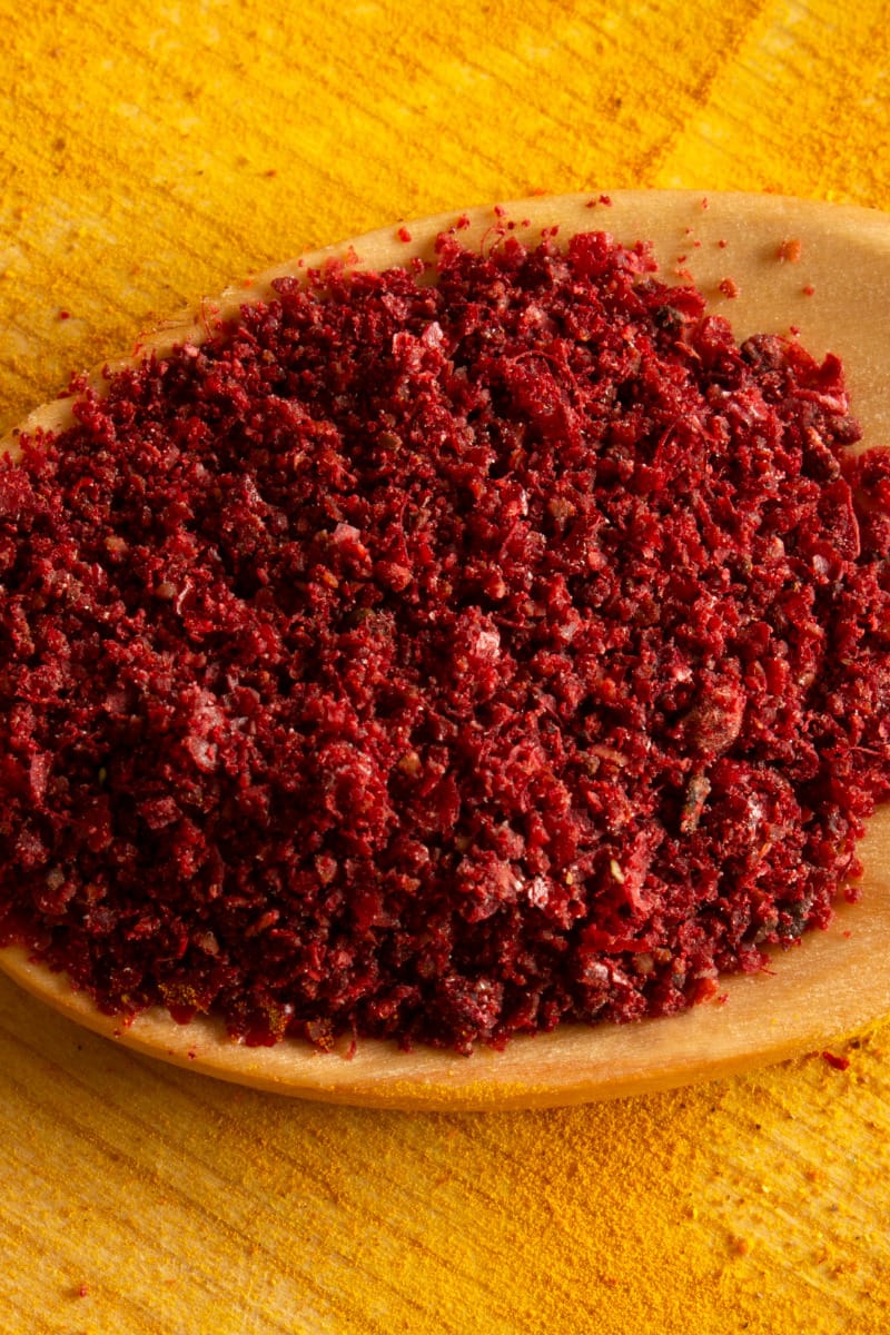 Ground sumac in a spoon on wooden table.