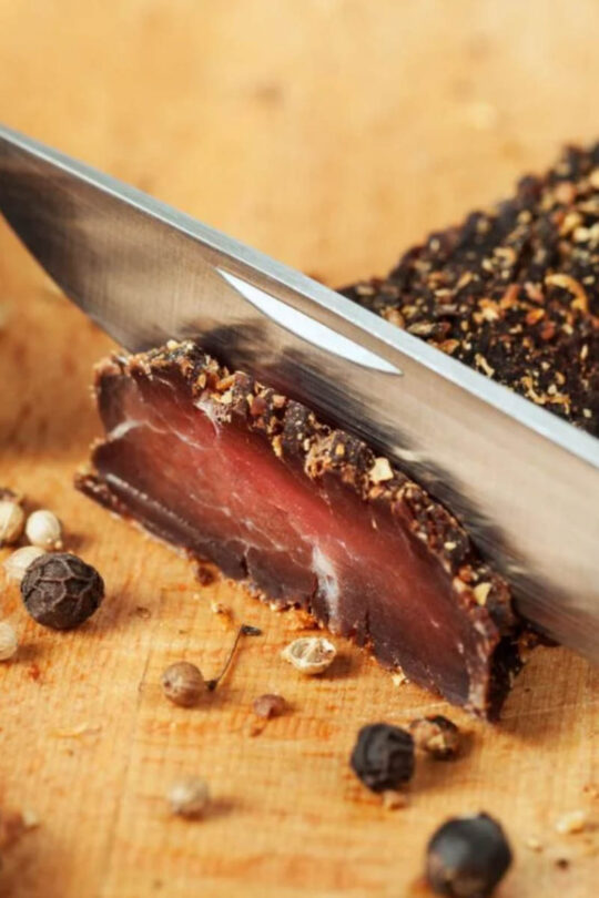 Knife slices through chunk of dried beef.