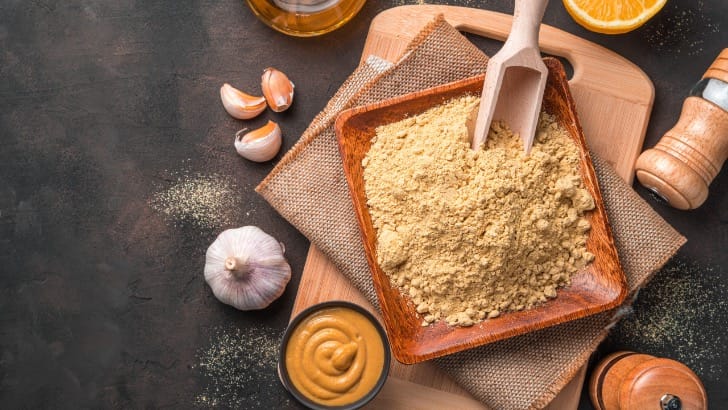 Top view of dry mustard in flat wooden bowl.