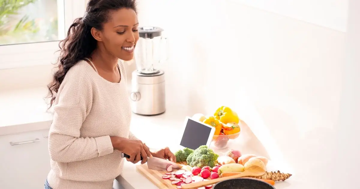 Woman smiles while chopping fresh vegetables in kitchen.