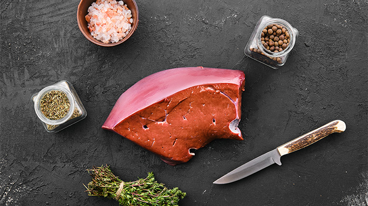 Raw beef liver on surface with spices.