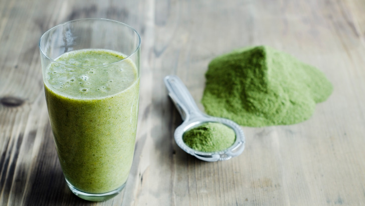 Moringa powder on spoon near moringa smoothie.