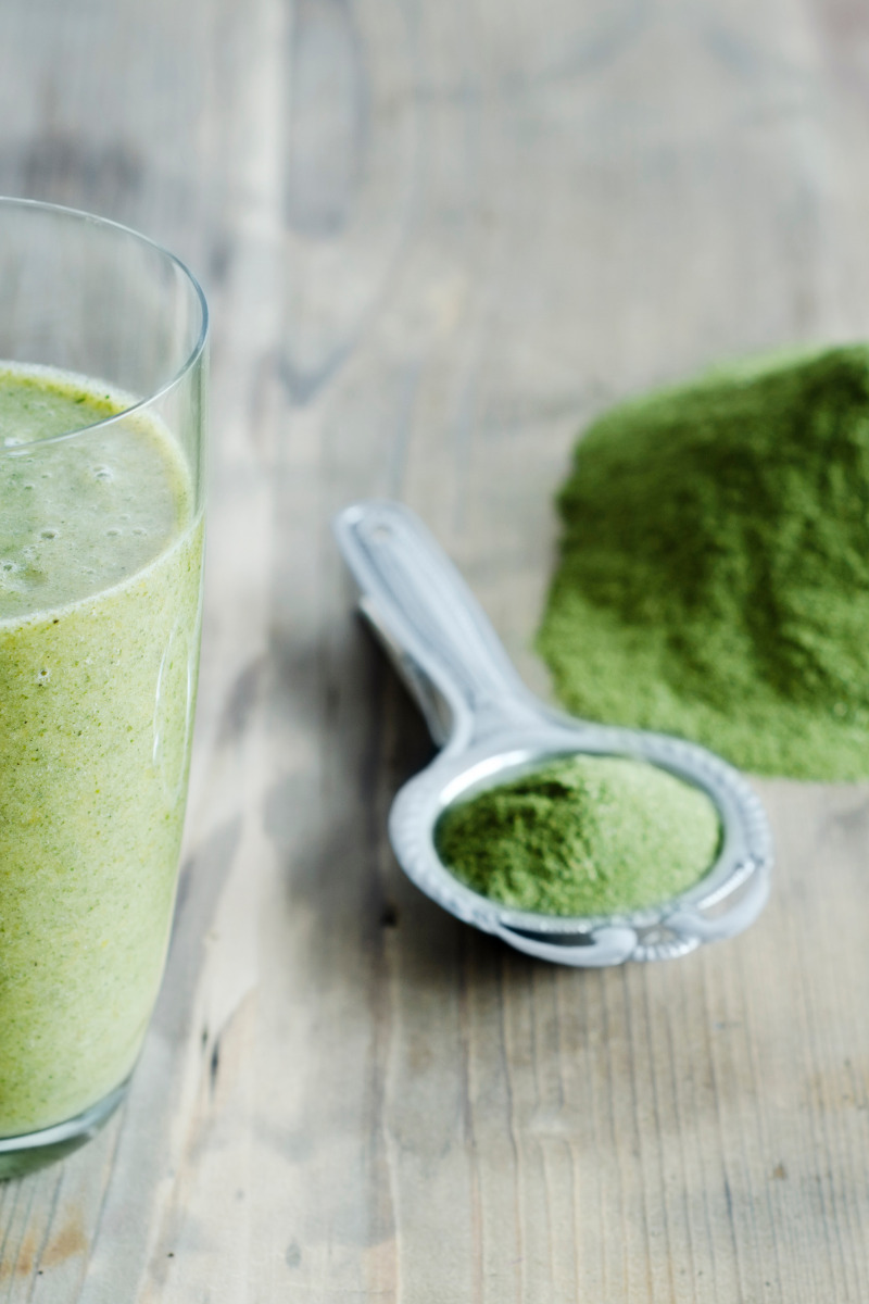 Moringa powder on spoon near moringa smoothie.