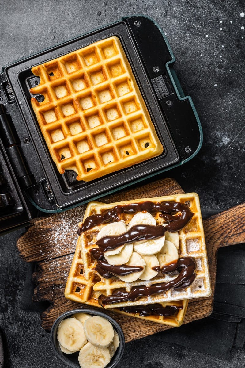 Prepared waffle next to waffle just cooked in waffle maker.