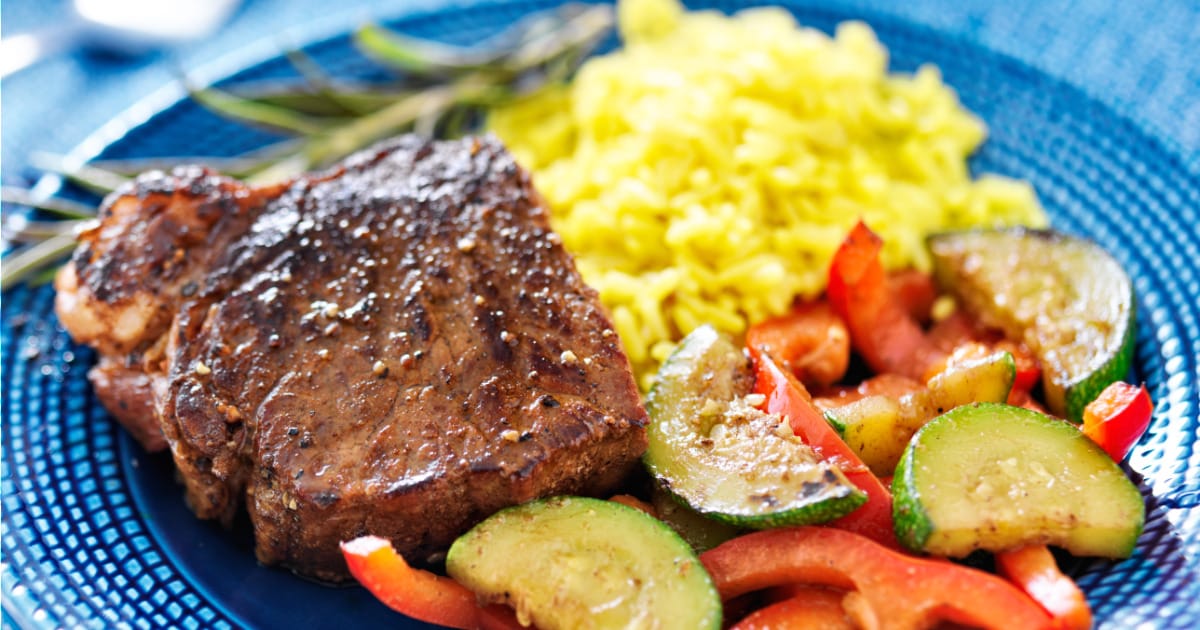 Marinated, oven-baked steak on plate with vegetables and rice.