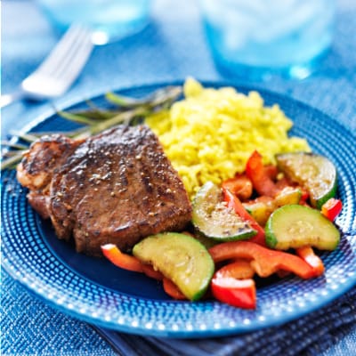 Marinated, oven-baked steak on plate with vegetables and rice.