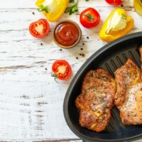 Baked pork chops in skillet on white wood surface.