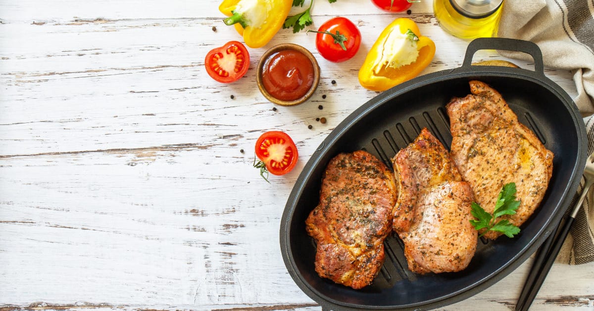 Baked pork chops in skillet on white wood surface.